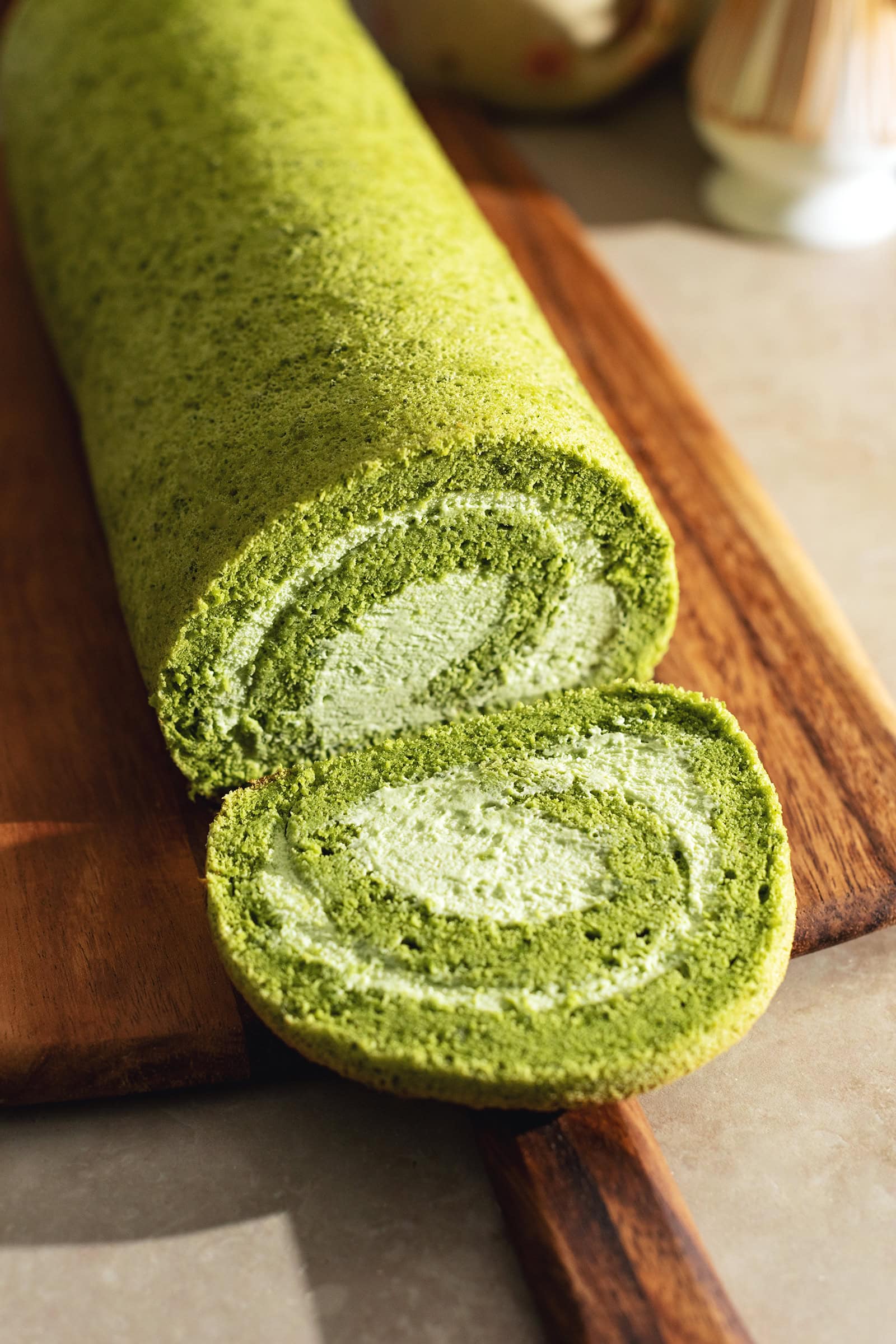 A slice cut from a matcha roll cake laying in front of the rest of the cake.