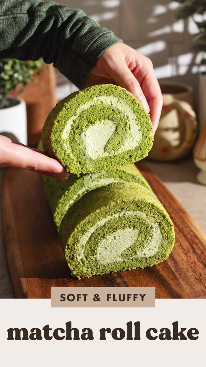 Hands holding a slice of matcha roll cake above the rest of the cake.