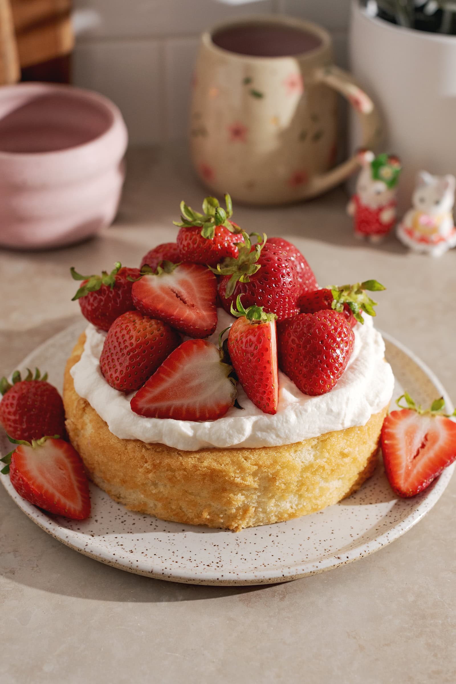 A mini strawberry cream cake on a plate with a pile of strawberries on top.