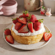 A mini strawberry cream cake on a plate with a pile of strawberries on top.