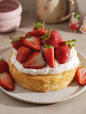 A mini strawberry cream cake on a plate with a pile of strawberries on top.