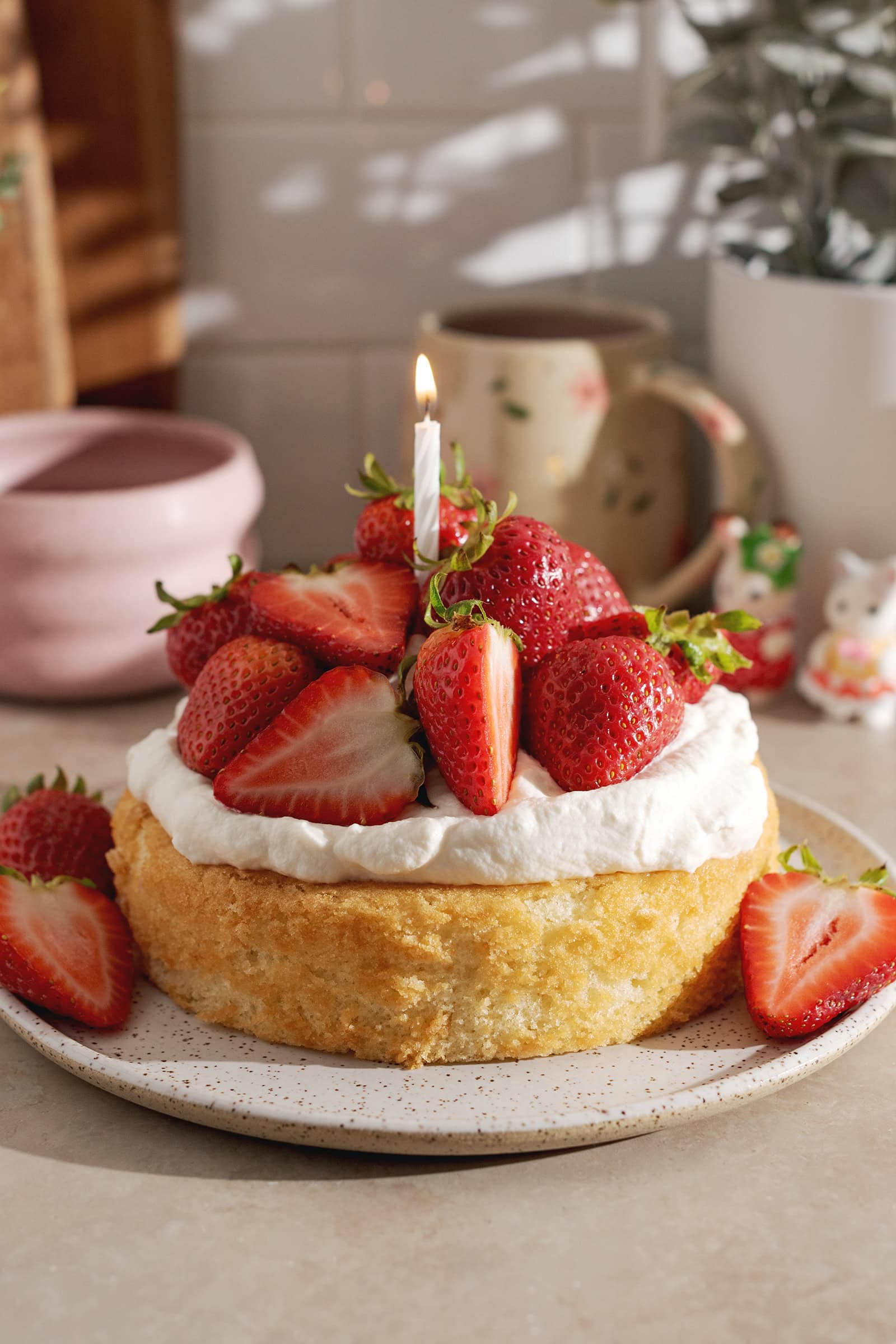 A mini strawberry cream cake with a lit birthday candle on top.