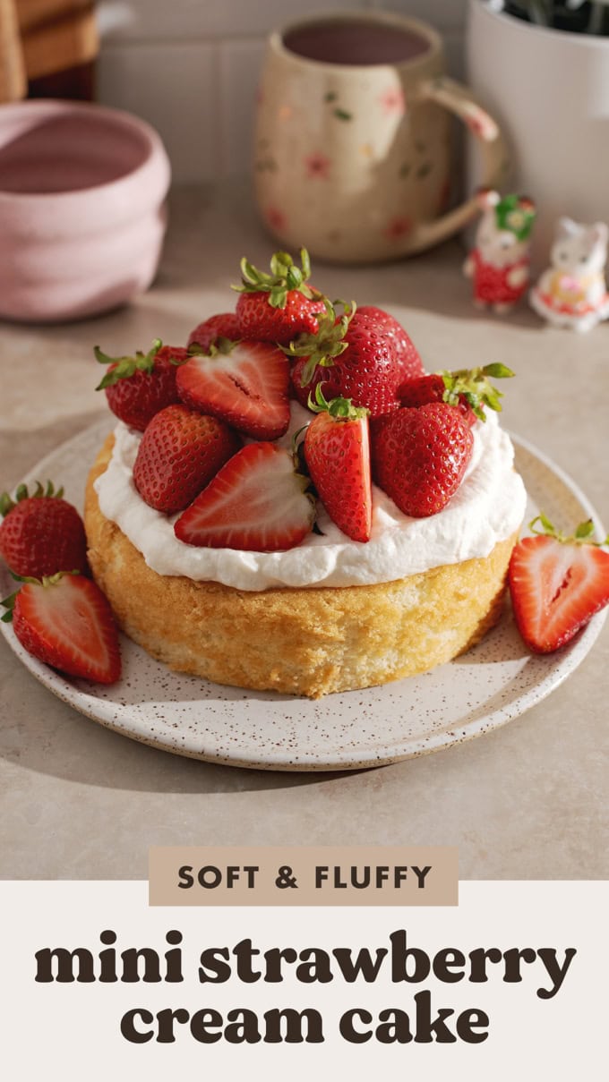 A mini strawberry cream cake on a plate with a pile of strawberries on top.