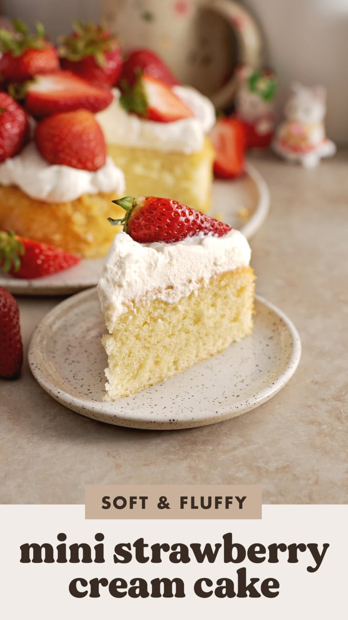 A slice of strawberry cream cake on a plate in front of the rest of the cake.