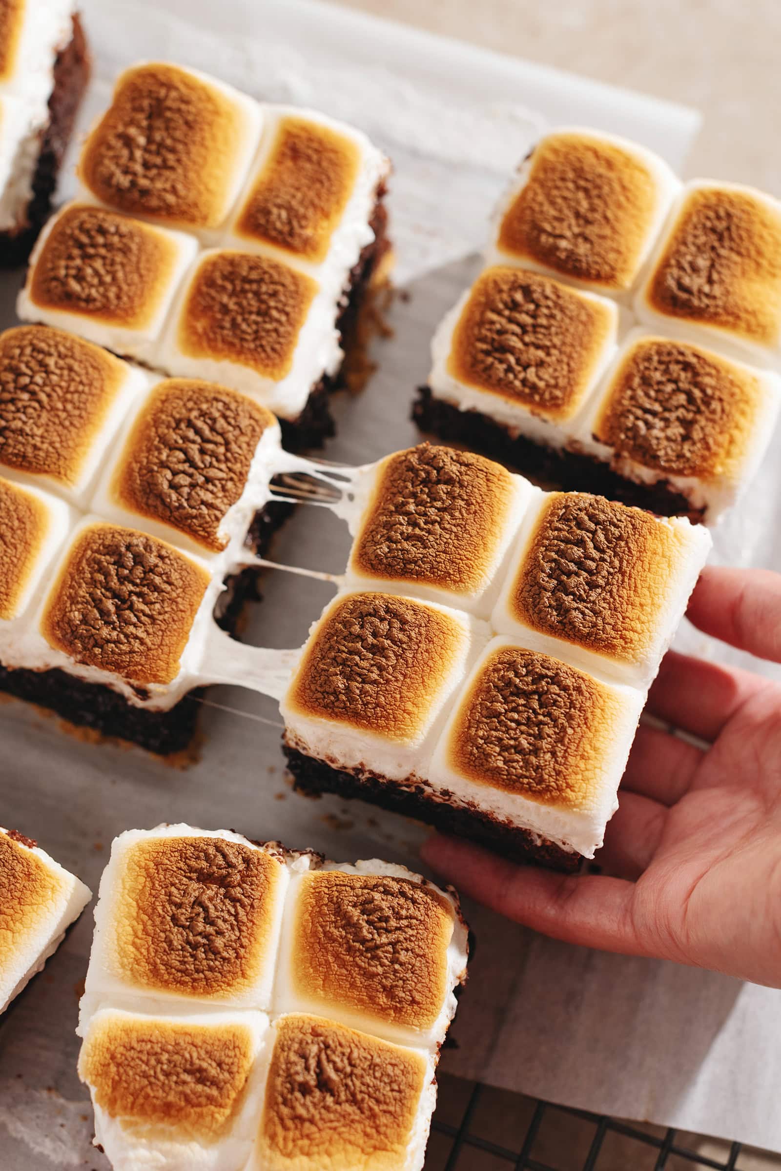 Hand pulling s'mores brownies apart with a gooey marshmallow pull in between them.
