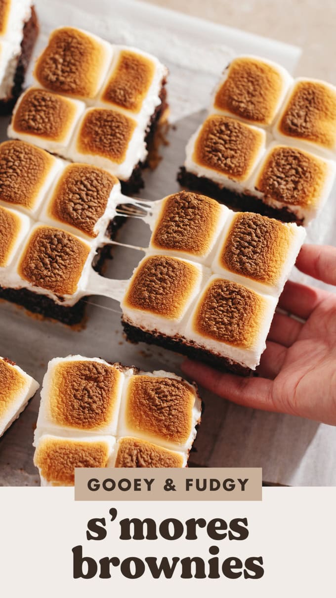 Hand pulling s'mores brownies apart with a gooey marshmallow pull in between them.