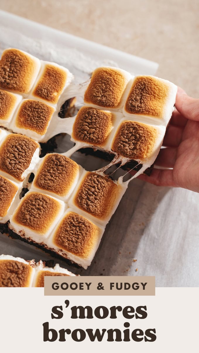 Hand pulling s'mores brownies apart with a gooey marshmallow pull in between them.