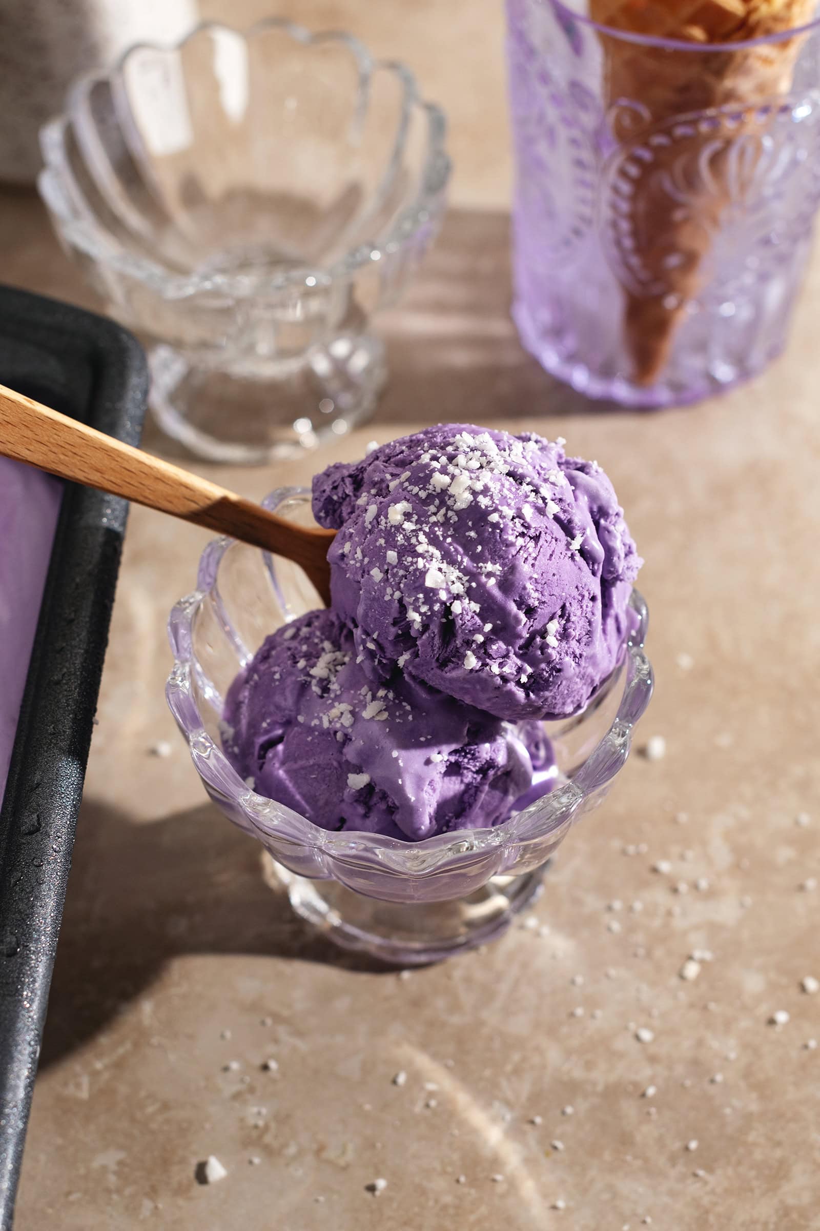 Two scoops of ube ice cream in a bowl with a spoon.