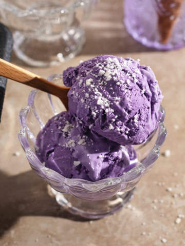 Two scoops of ube ice cream in a bowl with a spoon.