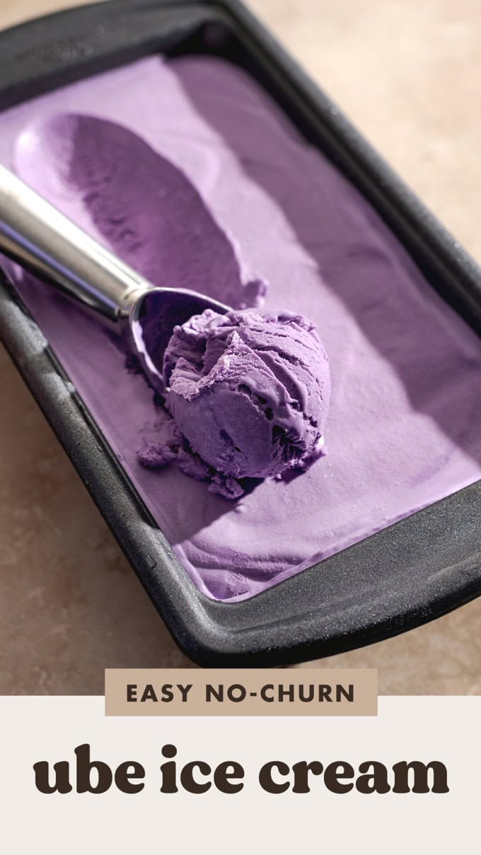 A ball of ice cream resting in an ice cream scooper in a pan of ice cream.