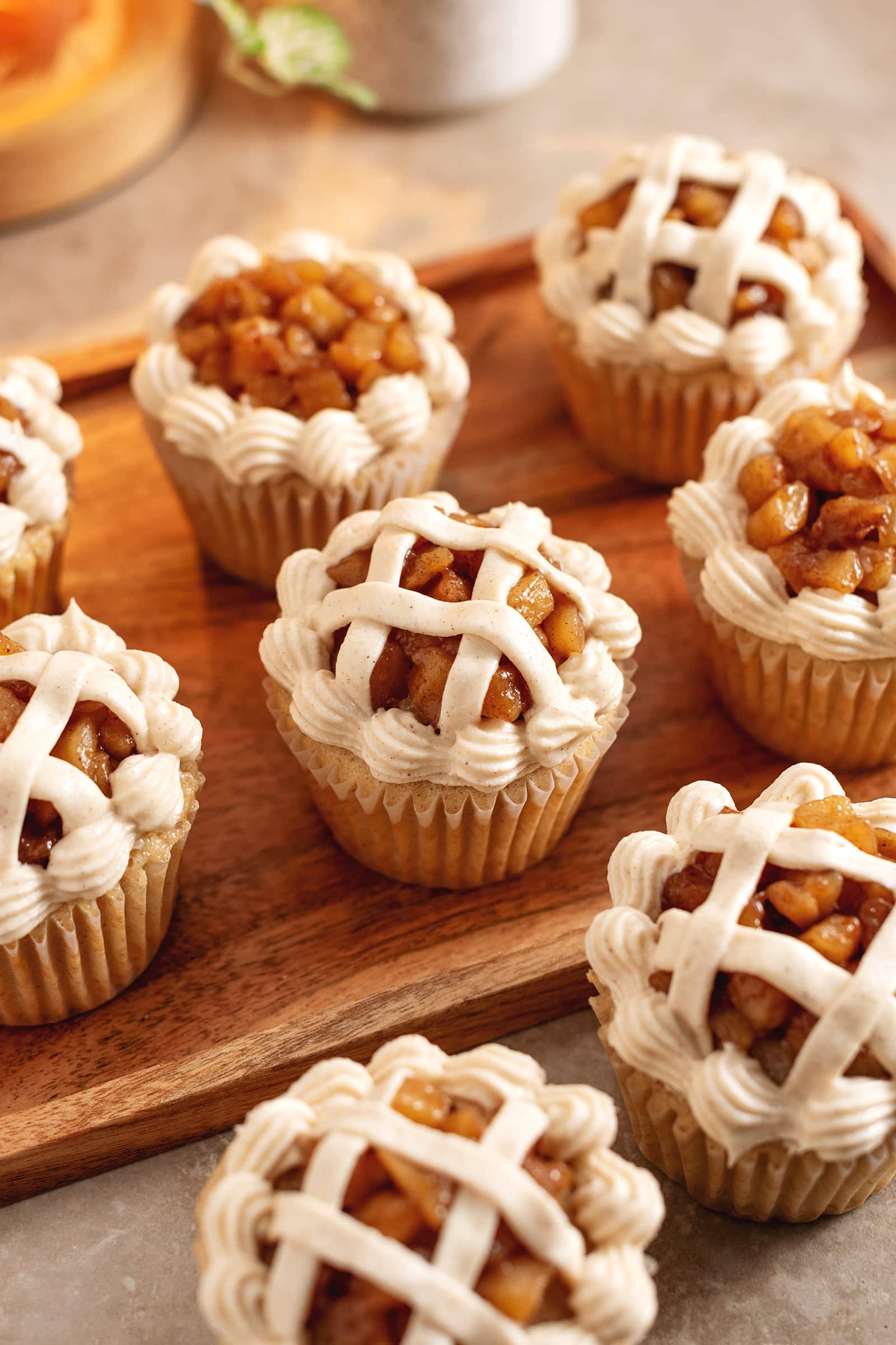 Several apple pie cupcakes decorated like a pie lattice scattered on a wooden tray.