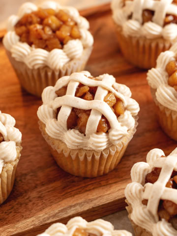 Several apple pie cupcakes decorated like a pie lattice scattered on a wooden tray.