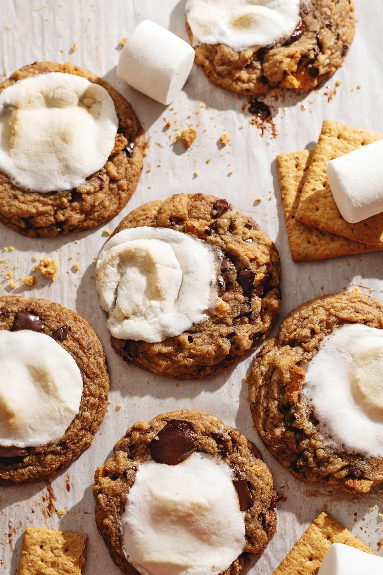 Several chocolate chip s'mores cookies scattered on parchment paper.