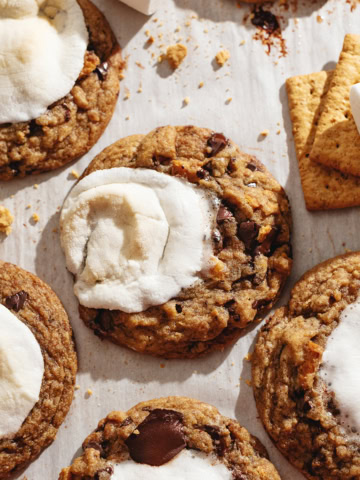 Several chocolate chip s'mores cookies scattered on parchment paper.