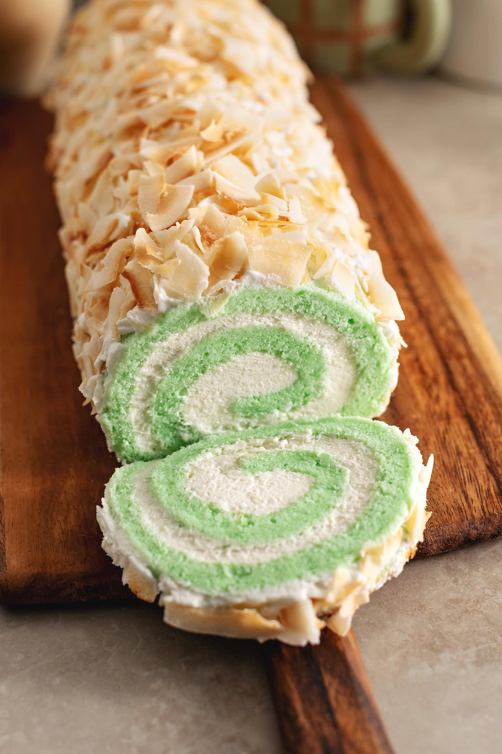 A slice of pandan swiss roll cake cut from the roll and laying in front of the rest of the roll cake.