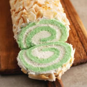 A slice of pandan swiss roll cake cut from the roll and laying in front of the rest of the roll cake.