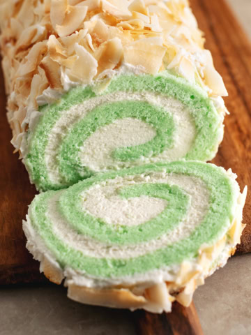A slice of pandan swiss roll cake cut from the roll and laying in front of the rest of the roll cake.