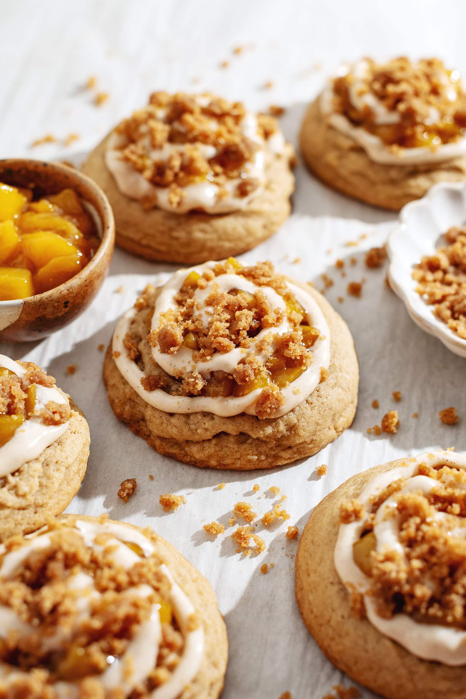 Side view of a peach cobbler cookie with a swirl of cream cheese on top surrounded by more cookies.