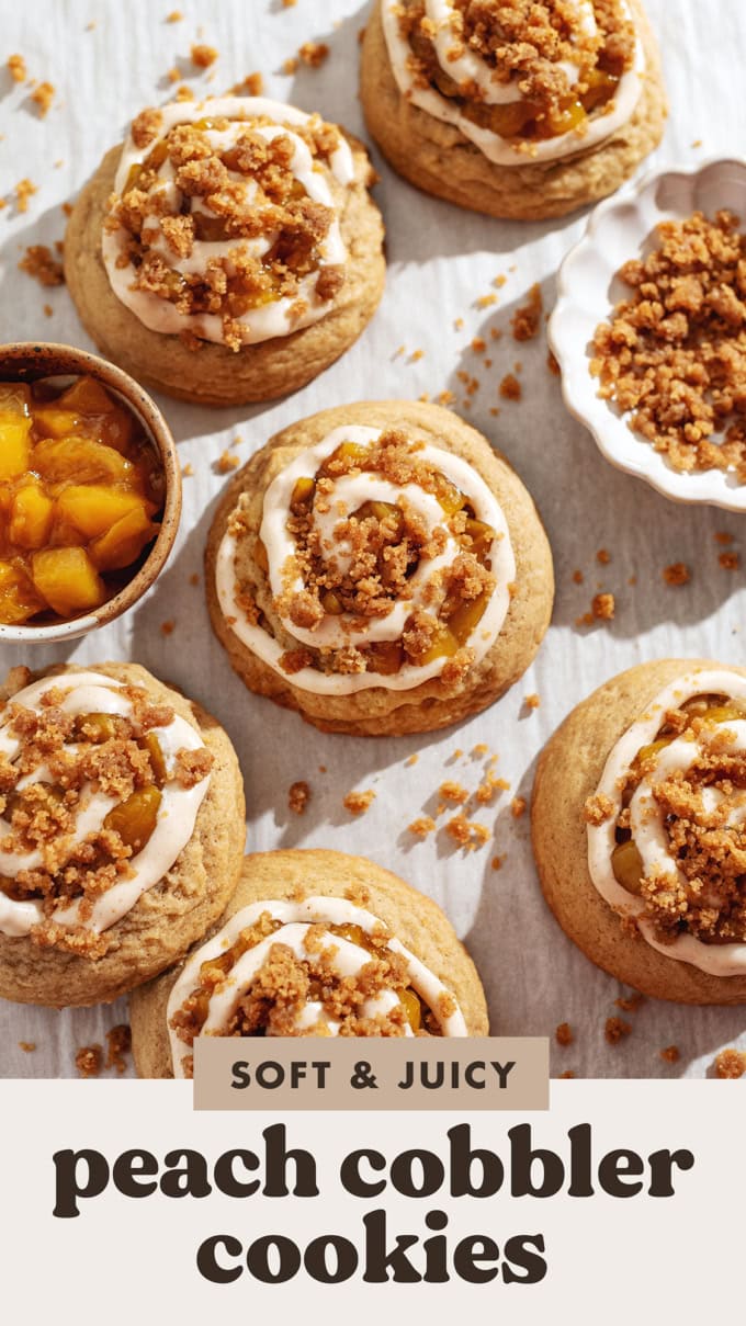 Several peach cobbler cookies scattered on parchment paper surrounded by baked crumble and a bowl of peach compote.