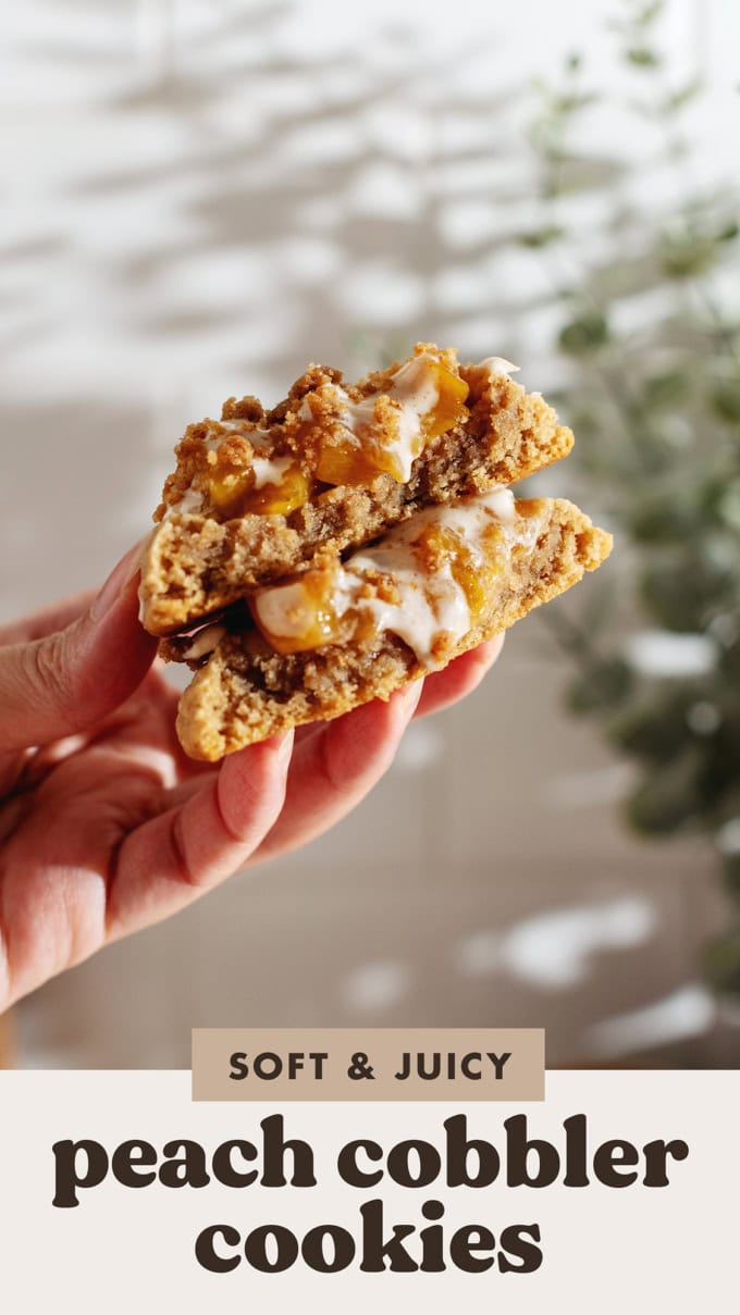 A hand holding two halves of a peach cobbler cookie to show the texture inside.