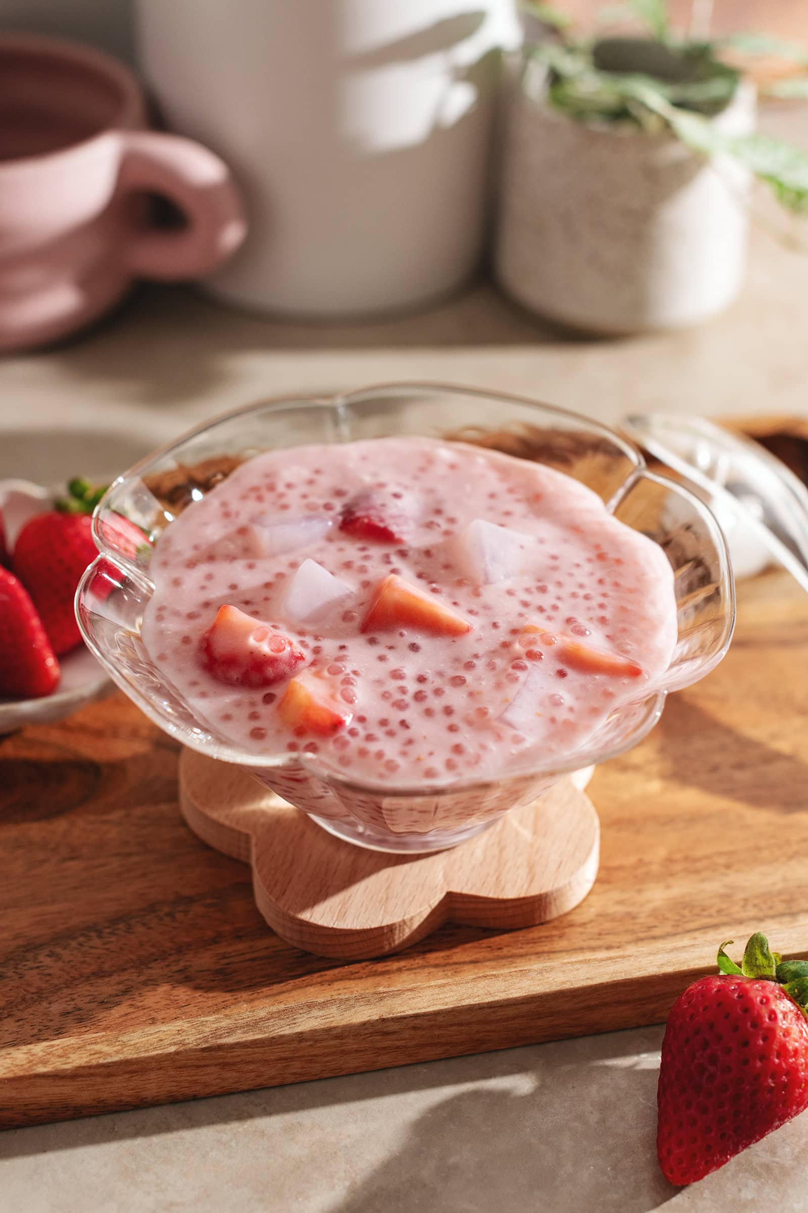 A glass bowl filled with strawberry sago on a wooden platter.