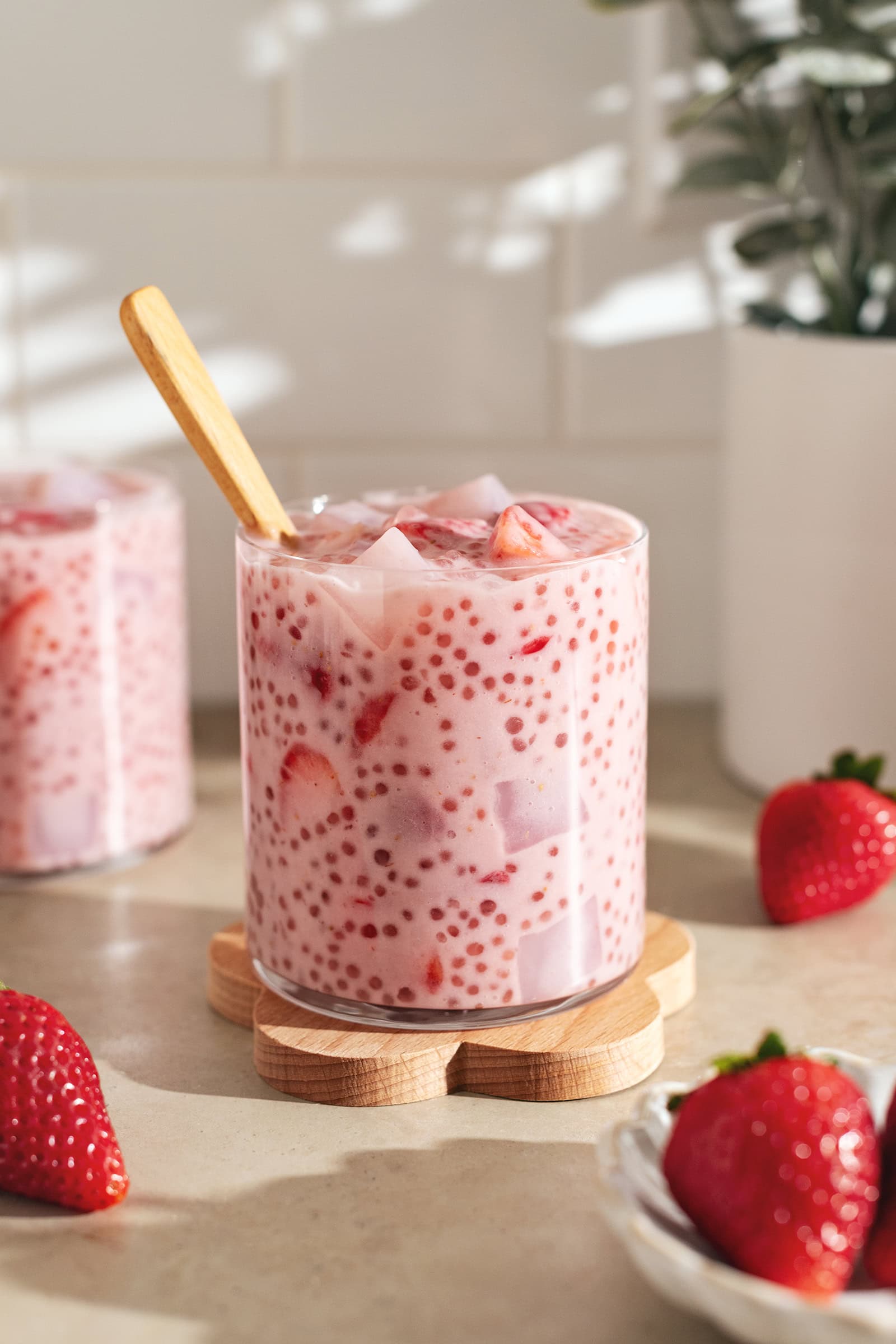 A glass cup filled with strawberry sago surrounded by strawberries.