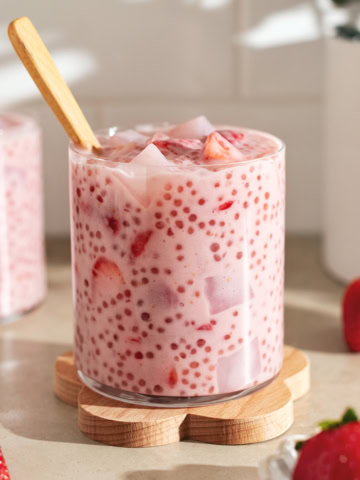 A glass cup filled with strawberry sago surrounded by strawberries.
