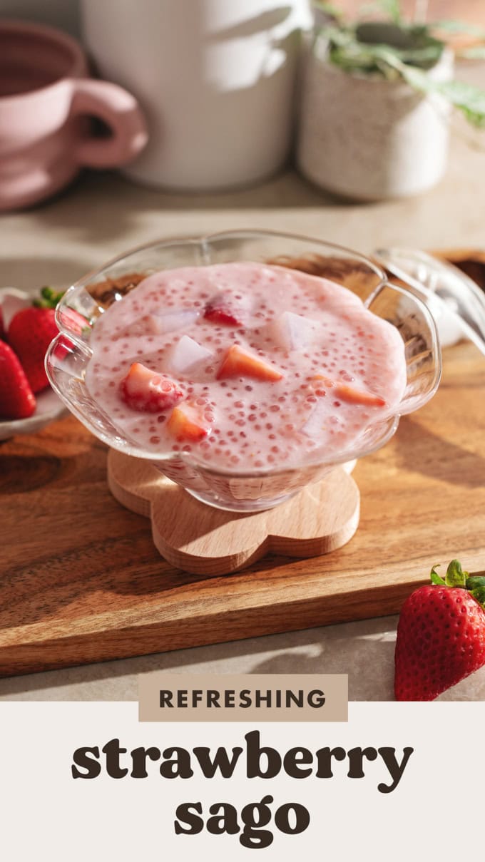 A glass bowl filled with strawberry sago on a wooden platter.