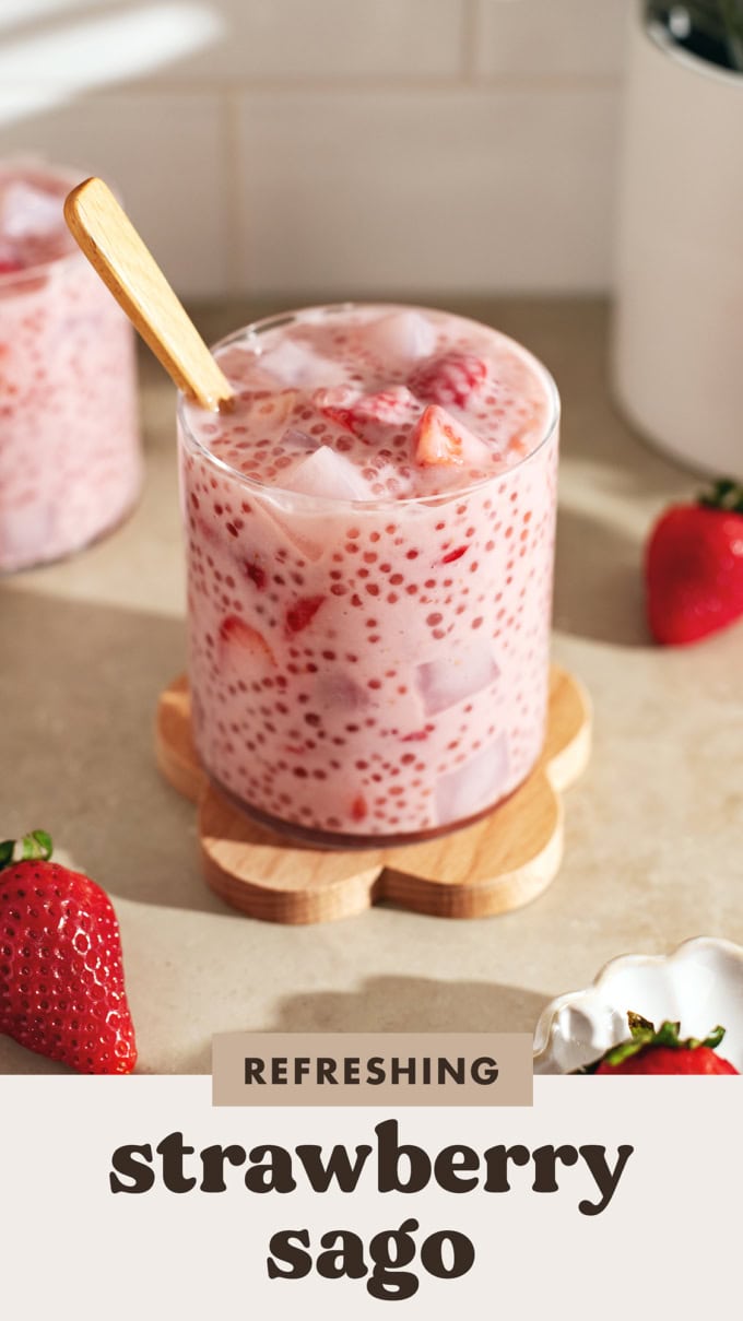 A glass cup filled with strawberry sago on a wooden coaster.