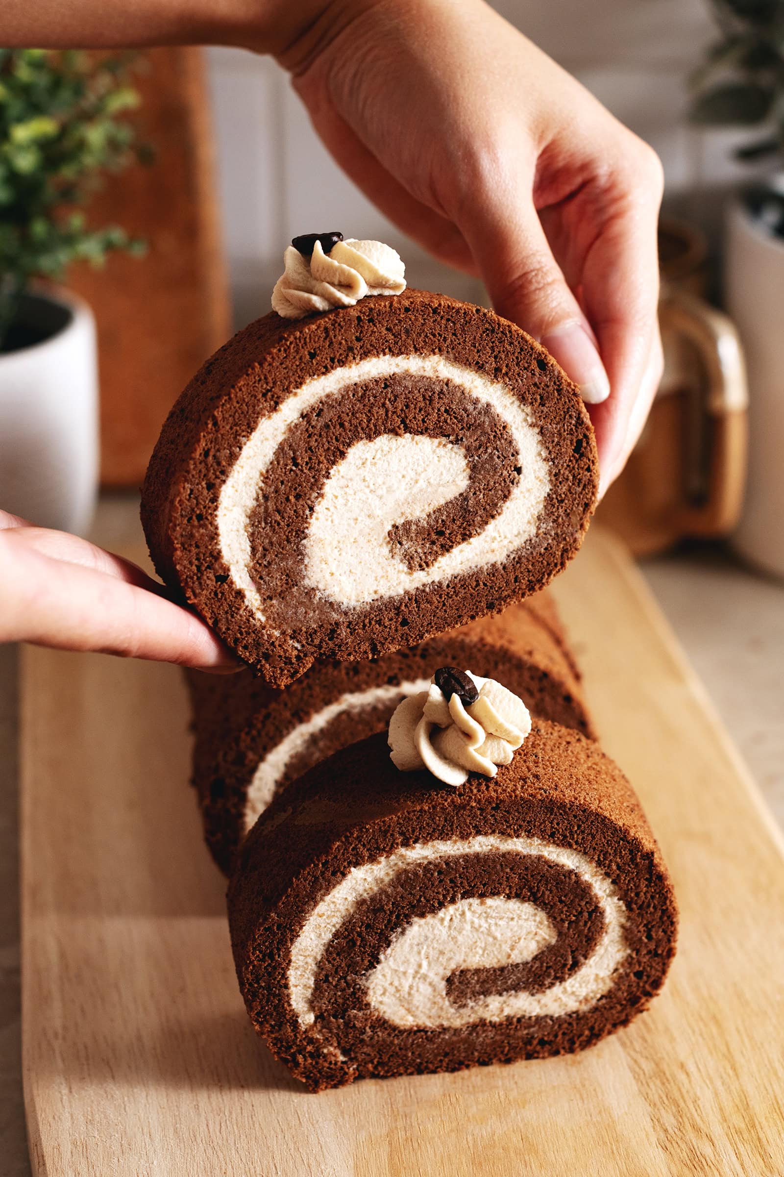 Hands lifting a slice of mocha roll cake up above the rest of the cake.