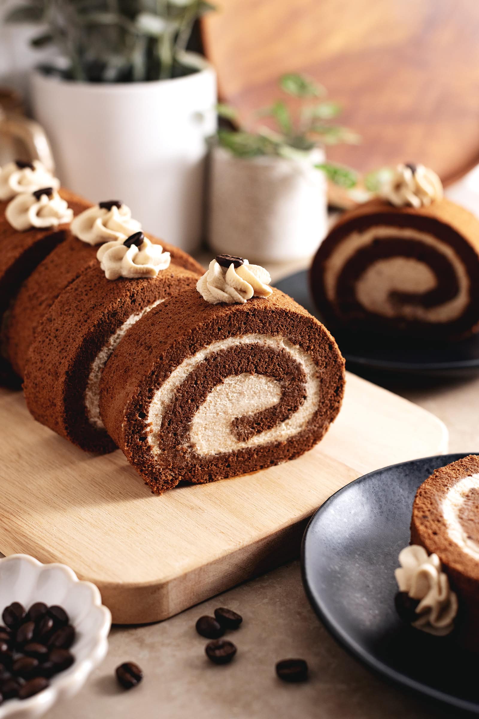Slices of mocha roll cake on a wooden platter with coffee beans scattered in front of them.