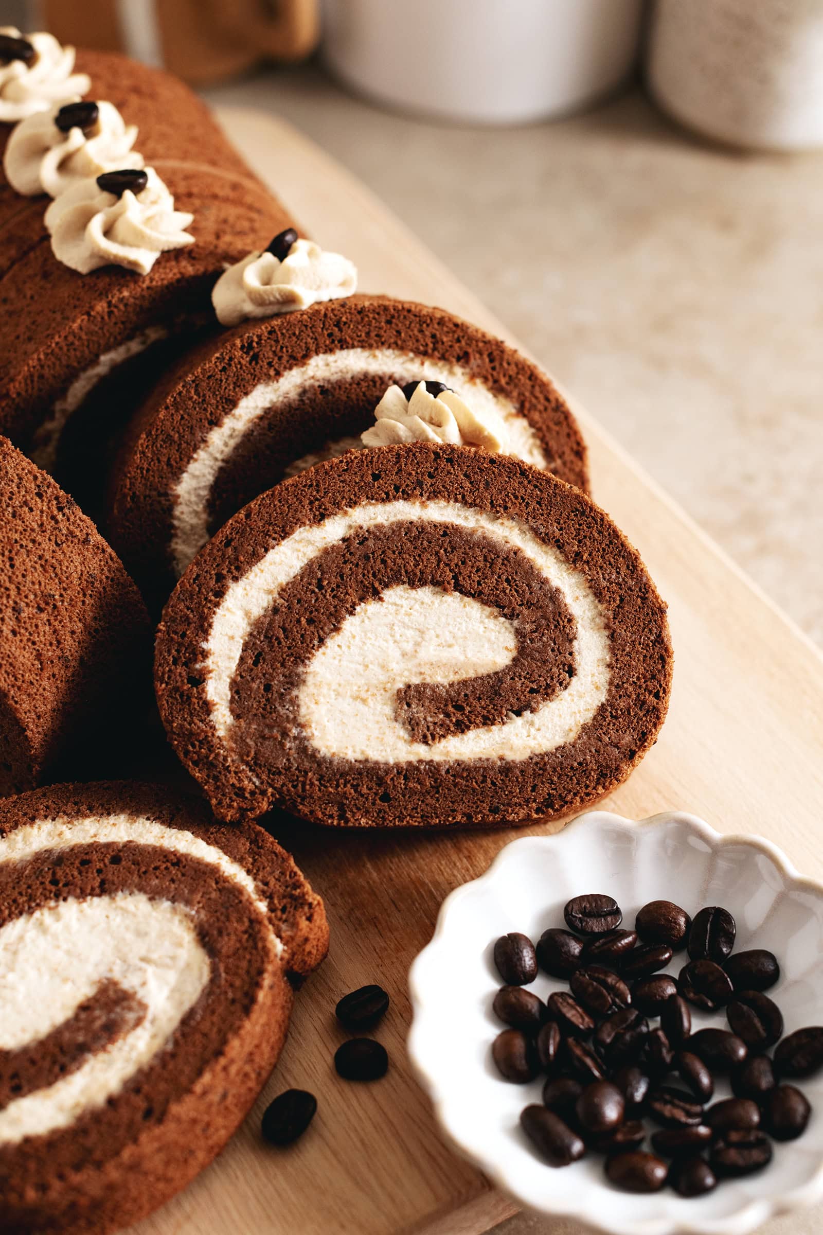 Slices of mocha roll cake arranged on a wooden platter with coffee beans in front of them.