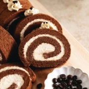 Slices of mocha roll cake arranged on a wooden platter with coffee beans in front of them.