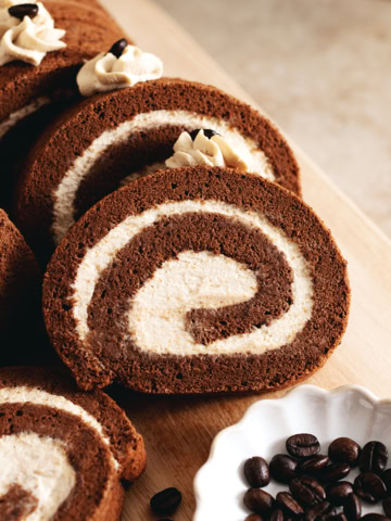 Slices of mocha roll cake arranged on a wooden platter with coffee beans in front of them.