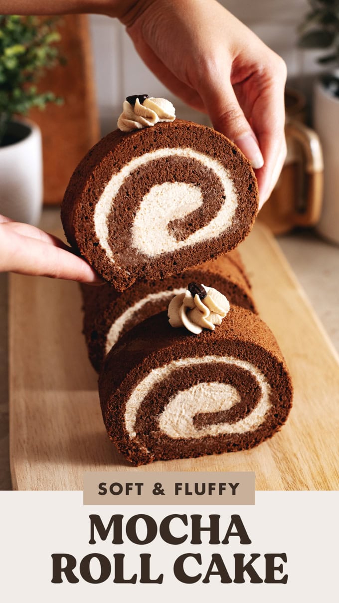 Hands lifting a slice of mocha roll cake up above the rest of the cake.