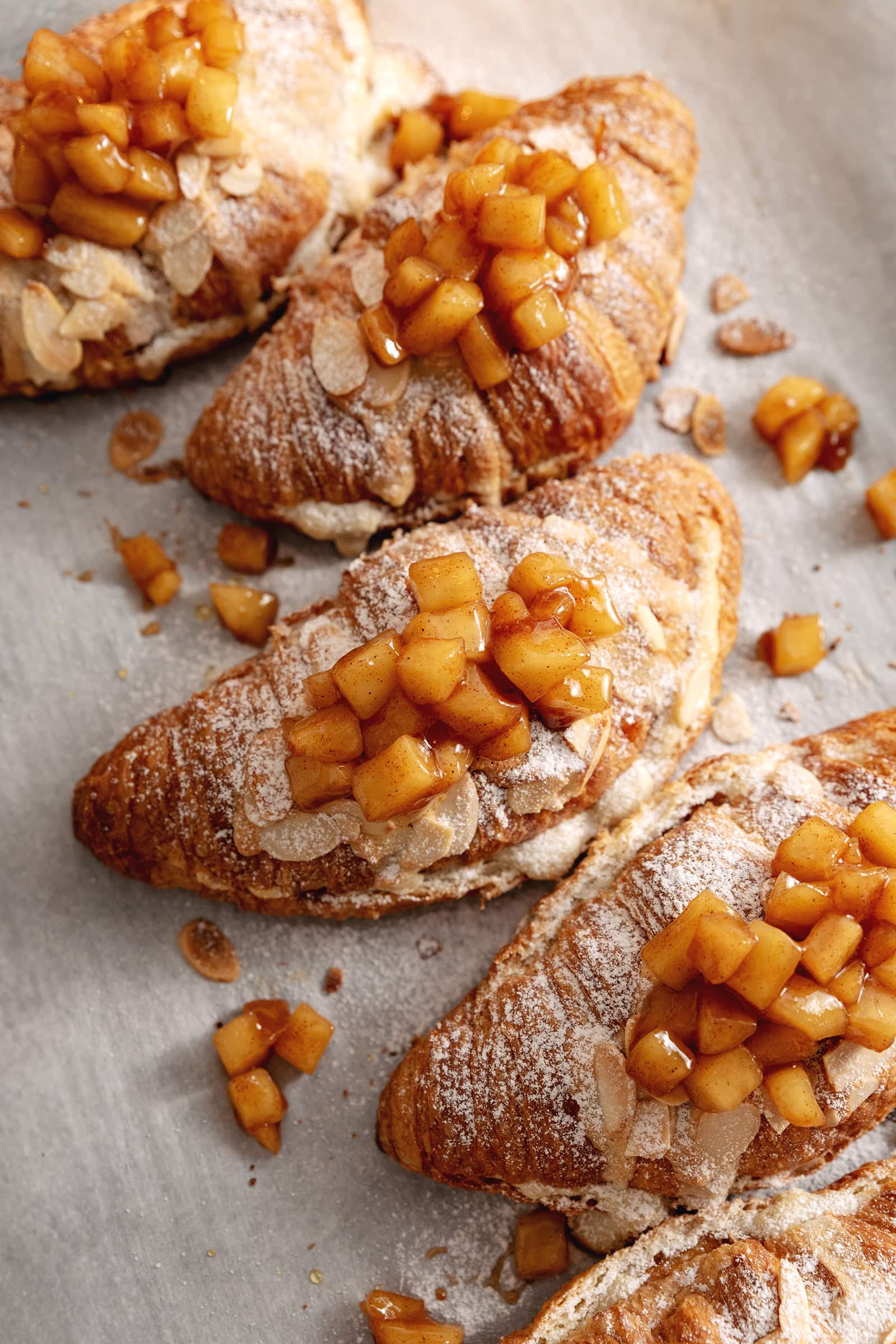 Several apple pie almond croissants lined up on parchment paper.