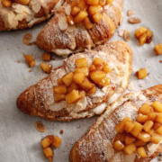 Several apple pie almond croissants lined up on parchment paper.