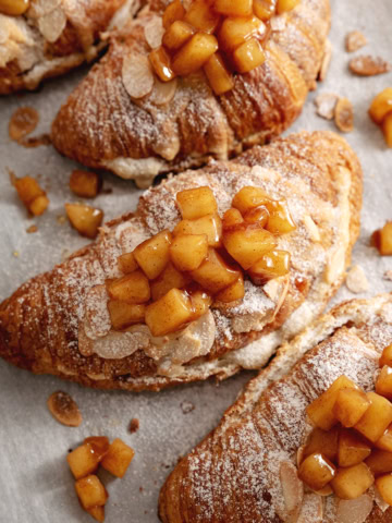 Several apple pie almond croissants lined up on parchment paper.