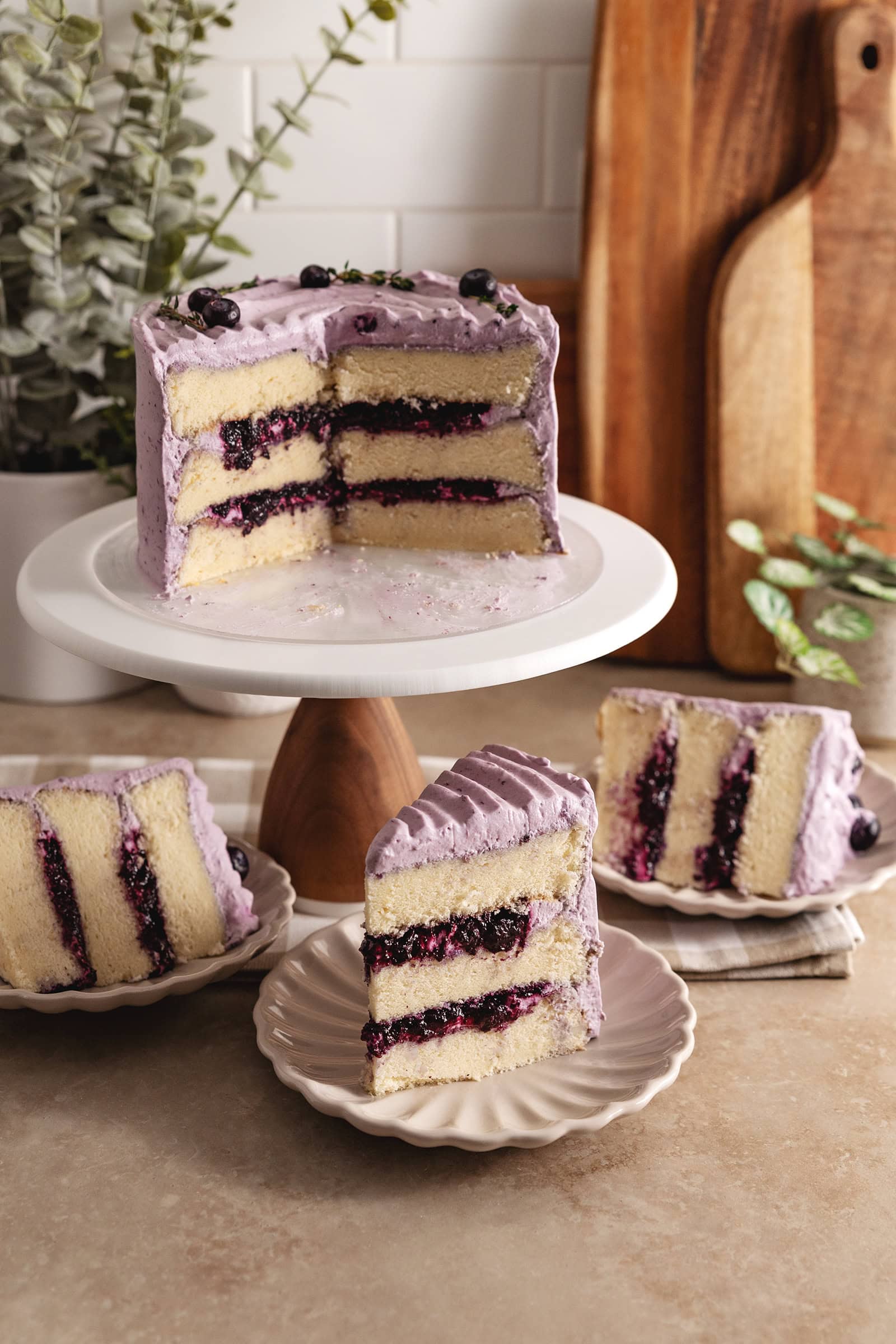 Slices of blueberry chiffon cake on plates surrounding the rest of the cake on a cake stand.
