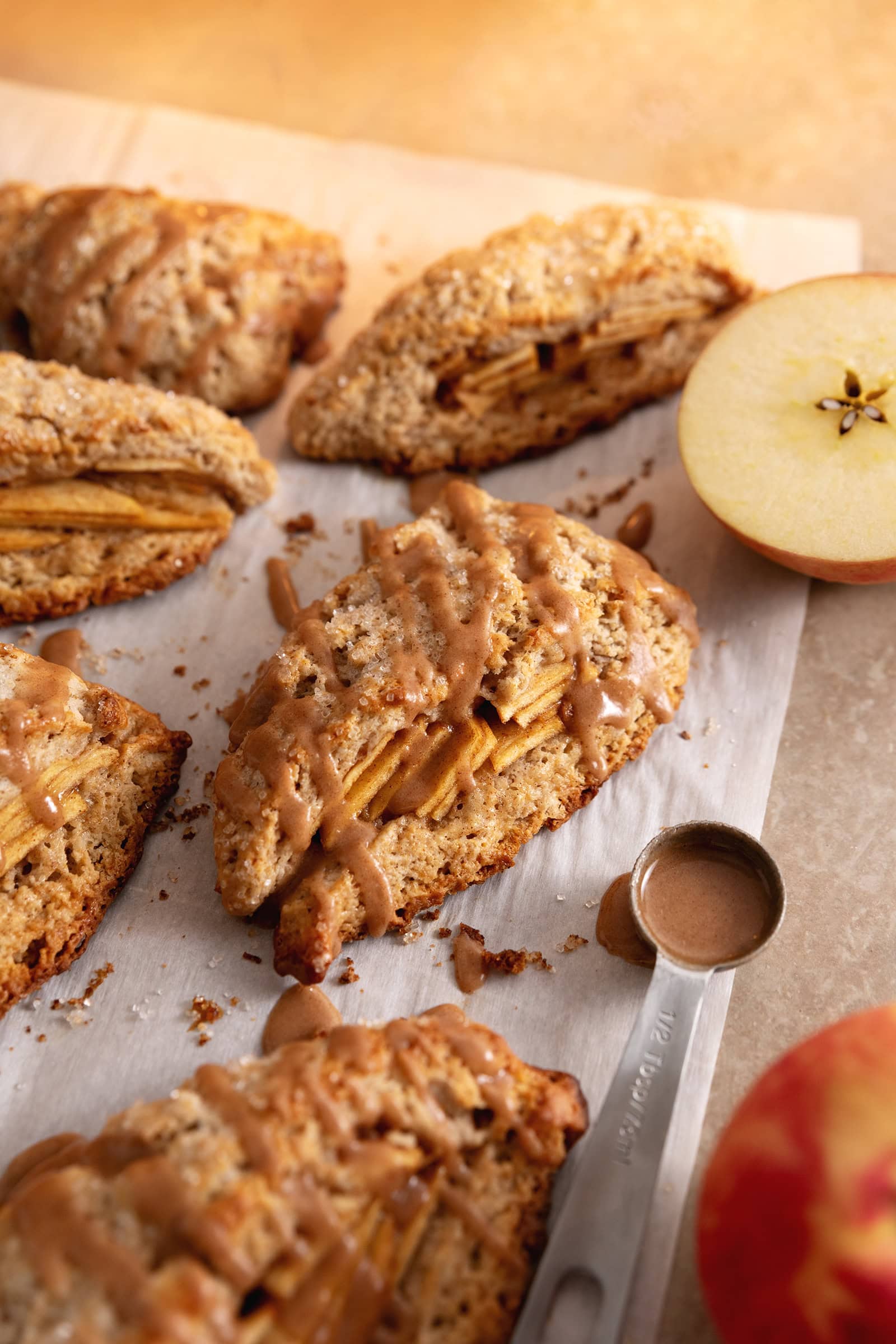 Cinnamon apple scones on parchment paper with a spoonful of icing next to them.