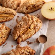 Cinnamon apple scones on parchment paper with a spoonful of icing next to them.