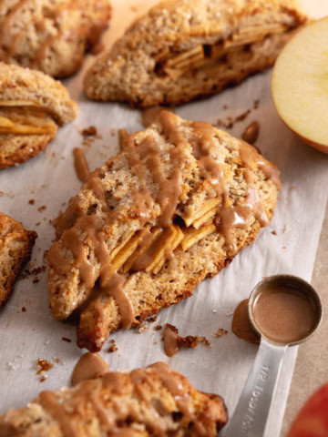 Cinnamon apple scones on parchment paper with a spoonful of icing next to them.