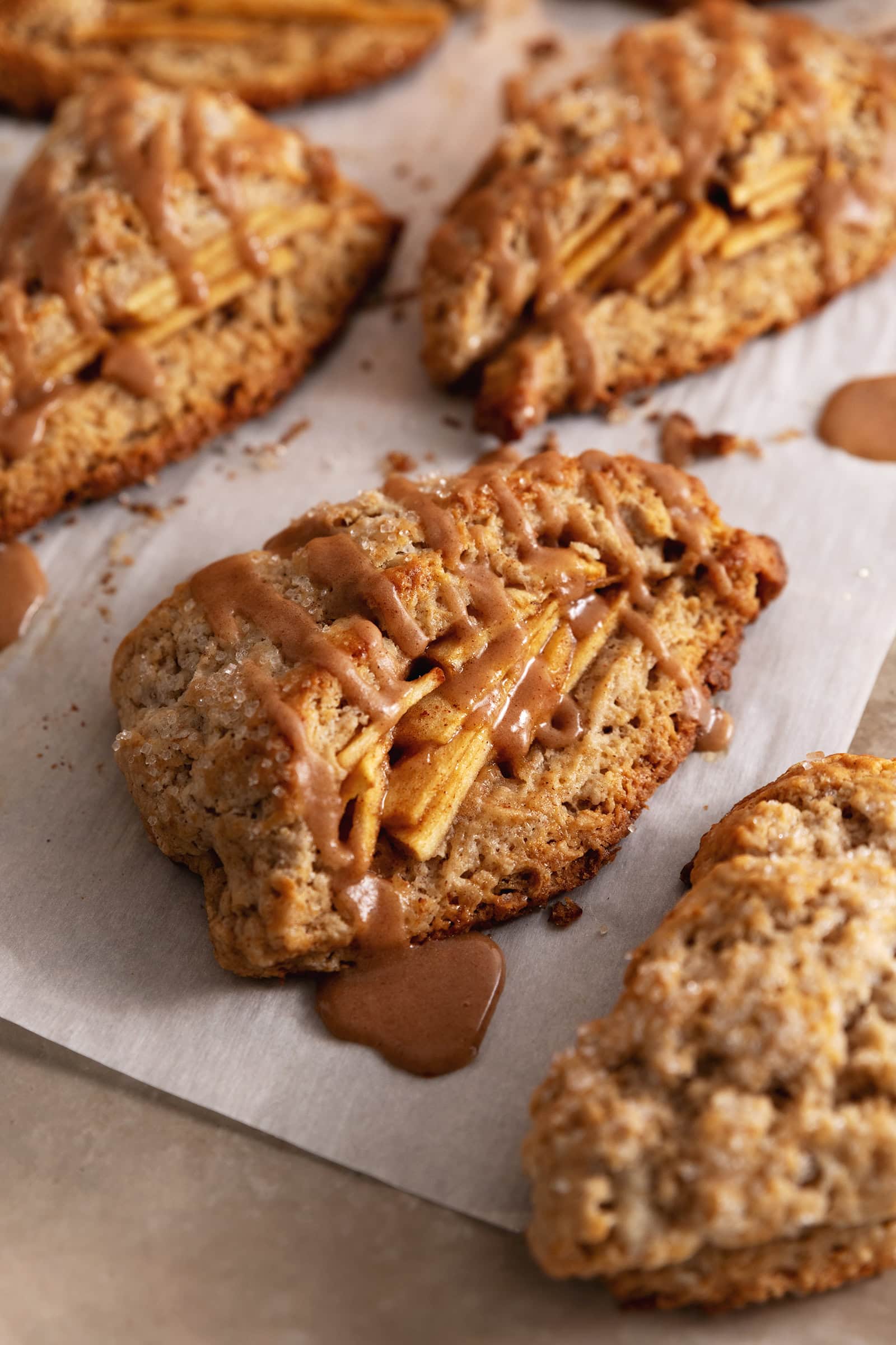 Cinnamon apple scones on parchment with maple glaze dripping off.