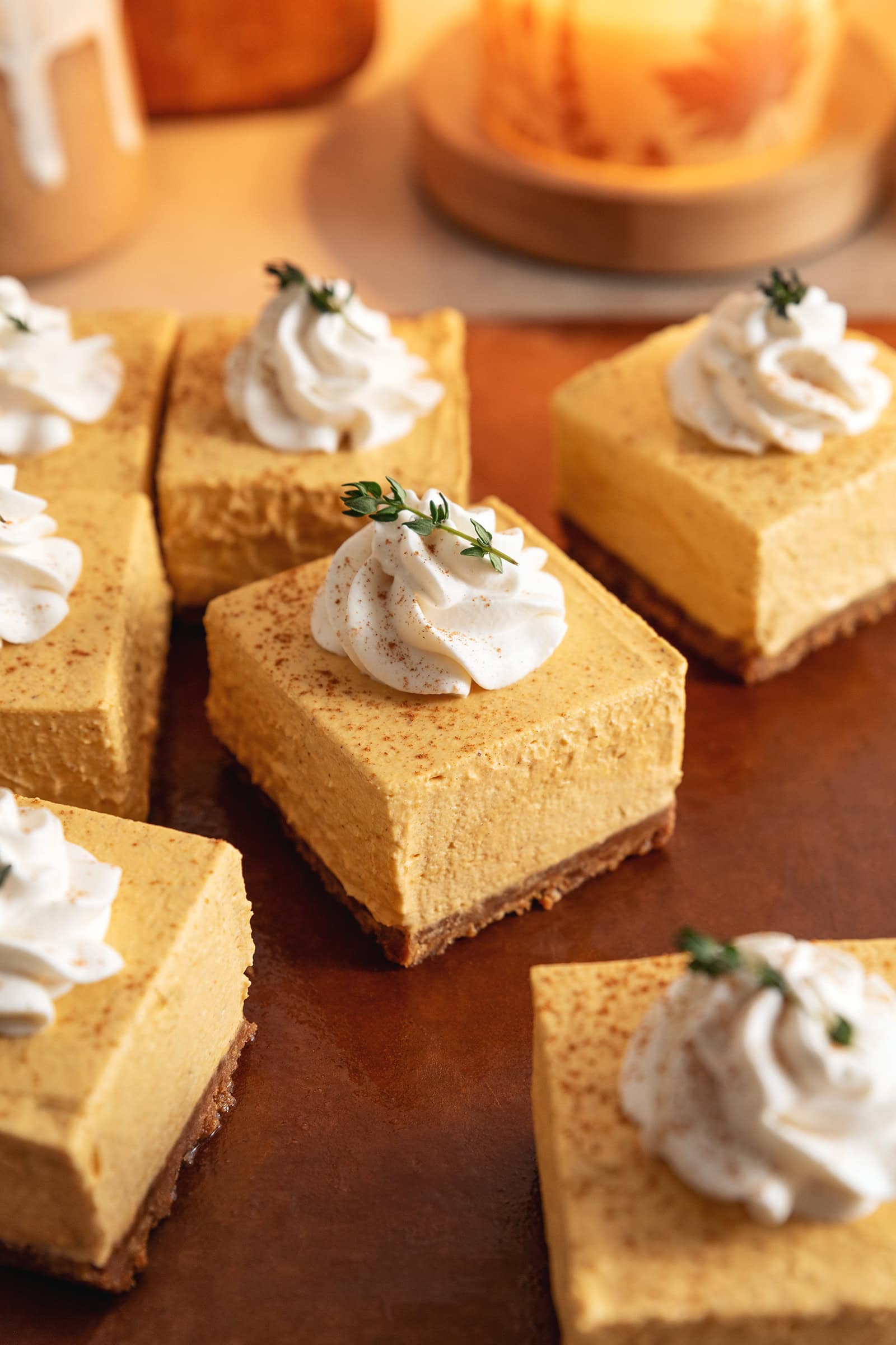 No-bake pumpkin cheesecake bars topped with a rosette of whipped cream scattered on a cutting board.