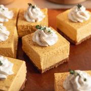 No-bake pumpkin cheesecake bars topped with a rosette of whipped cream scattered on a cutting board.