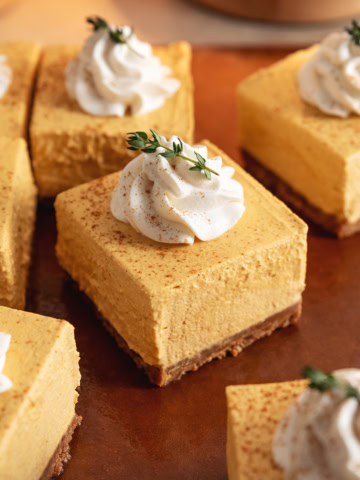 No-bake pumpkin cheesecake bars topped with a rosette of whipped cream scattered on a cutting board.