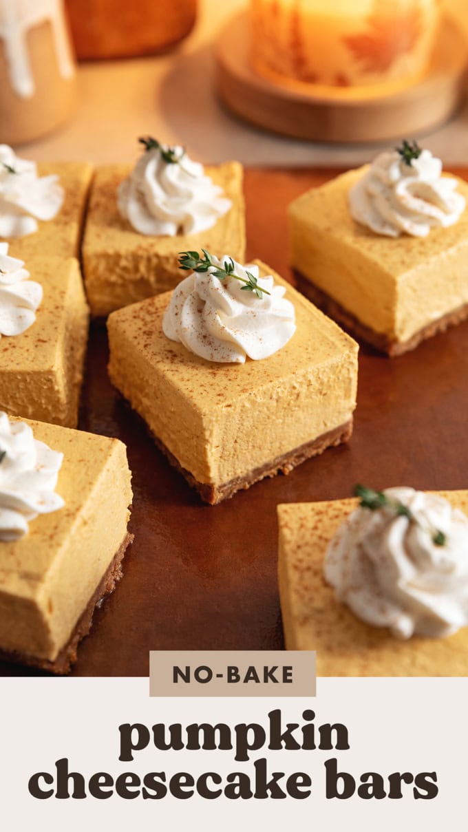 No-bake pumpkin cheesecake bars topped with a rosette of whipped cream scattered on a cutting board.