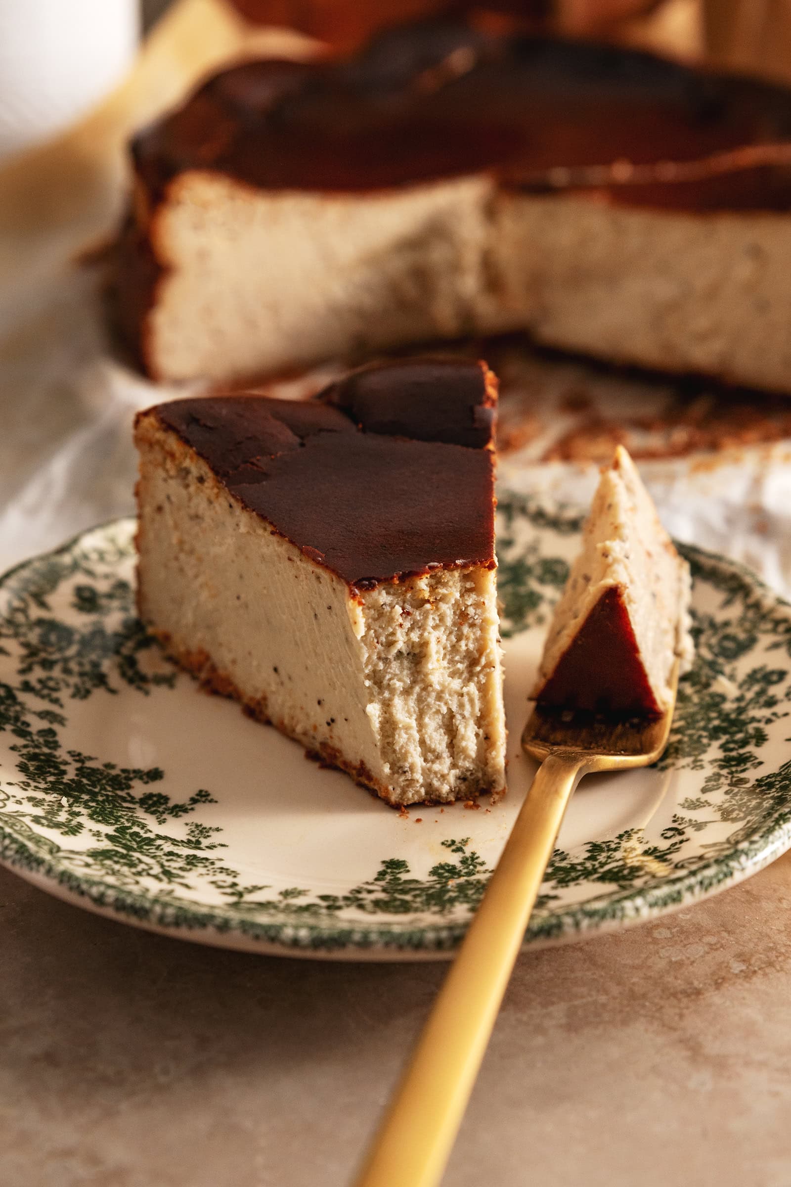 A slice of earl grey basque cheesecake and a forkful of cheesecake next to it on a plate.