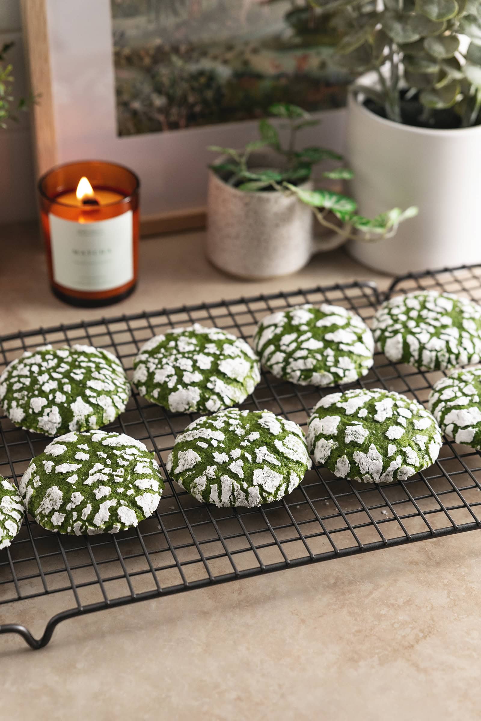 Matcha crinkle cookies lined up on a wire rack on a kitchen counter.