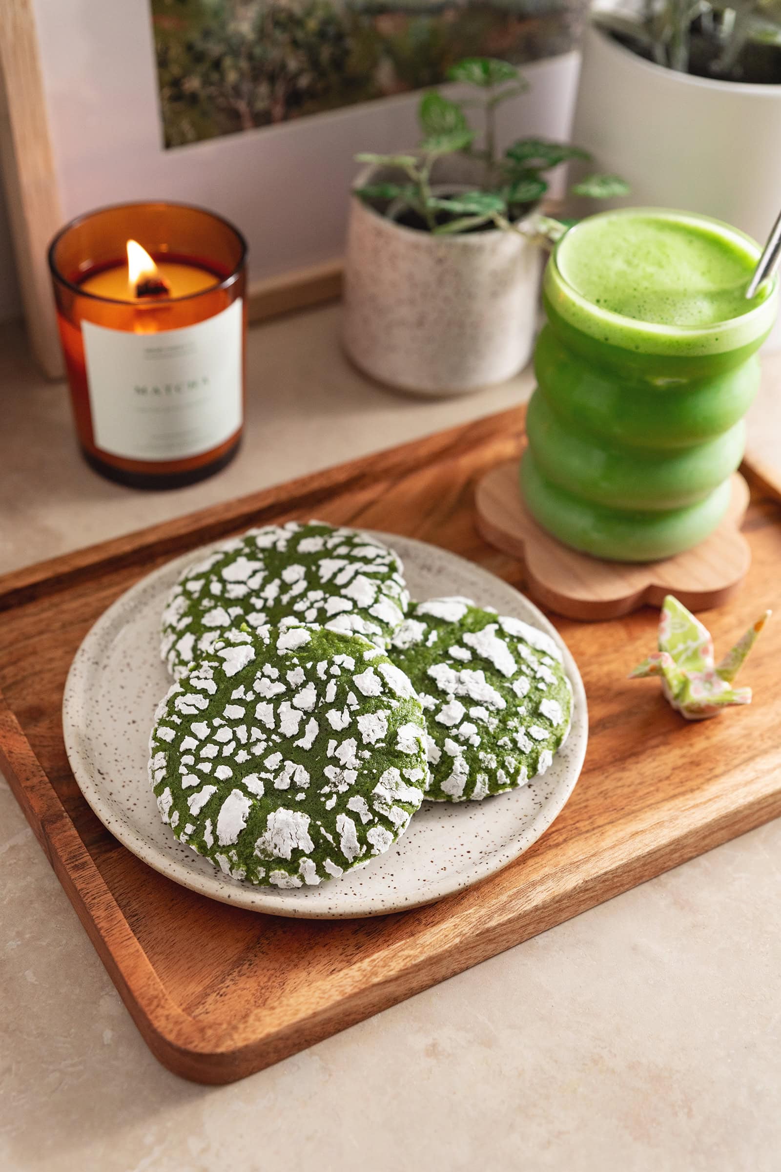 Three matcha crinkle cookies on a wooden platter with a glass of matcha latte next to it.
